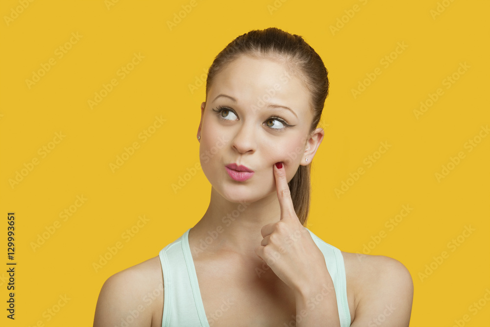 Thoughtful young woman looking sideways over yellow background Thoughtful young woman looking sideways over yellow background