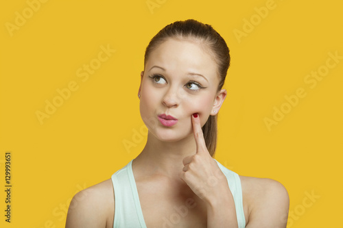 Thoughtful young woman looking sideways over yellow background