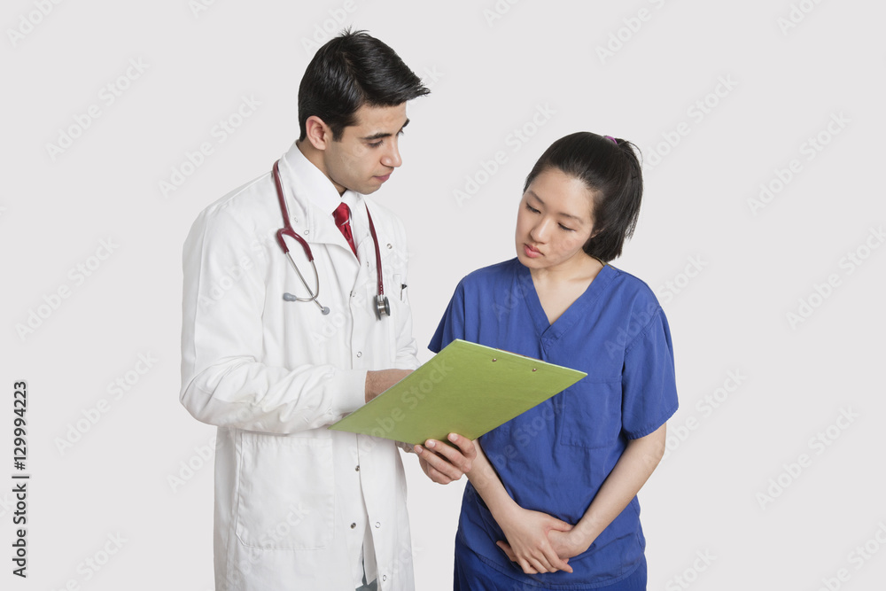 Doctor discussing medical report with female nurse over gray background Doctor discussing medical report with female nurse over gray background