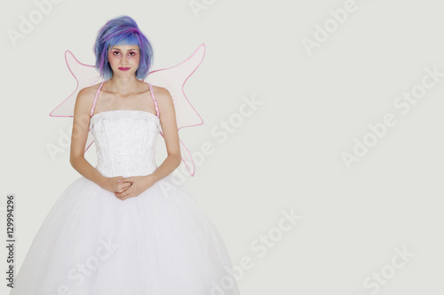 Portrait of beautiful young woman dressed as angel with dyed hair against gray background