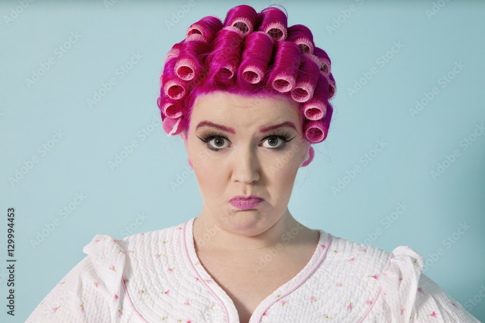 Portrait of young woman grimacing with hair curlers over colored background Portrait of young woman grimacing with hair curlers over colored background