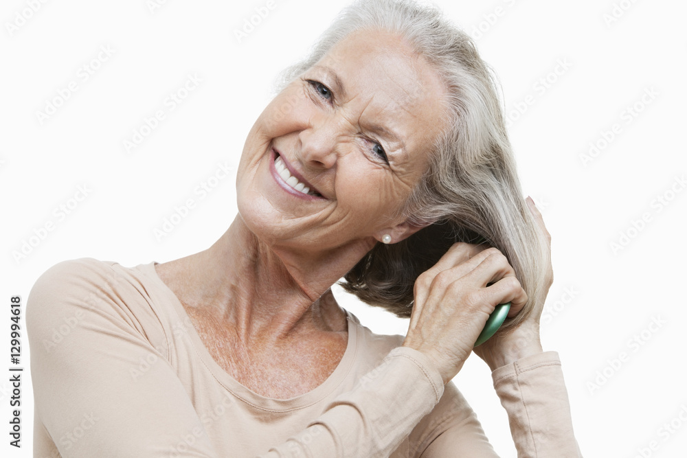 Portrait of smiling senior woman combing her hair against white background Portrait of smiling senior woman combing her hair against white background