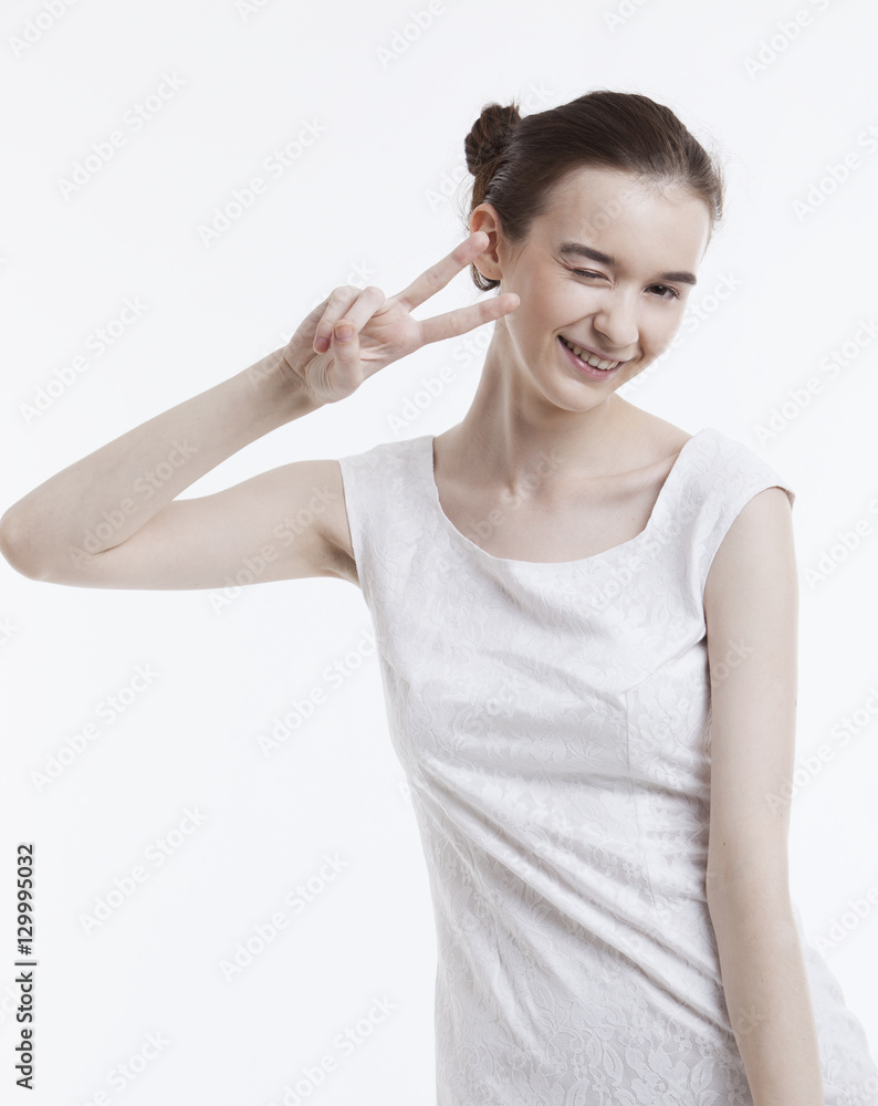 Portrait of young woman in dress gesturing peace sign over white background Portrait of young woman in dress gesturing peace sign over white background