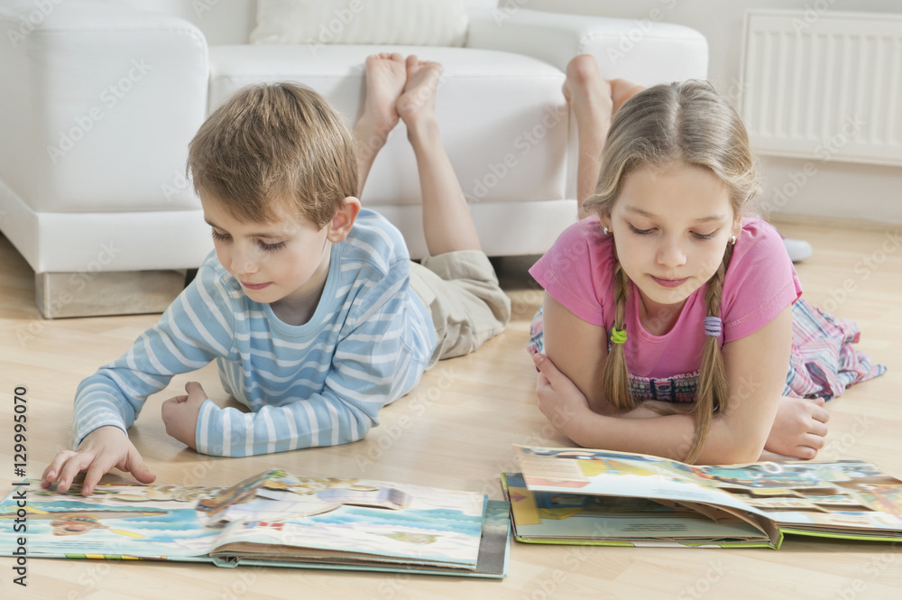 Siblings reading story books on floor in the living room Siblings reading story books on floor in the living room
