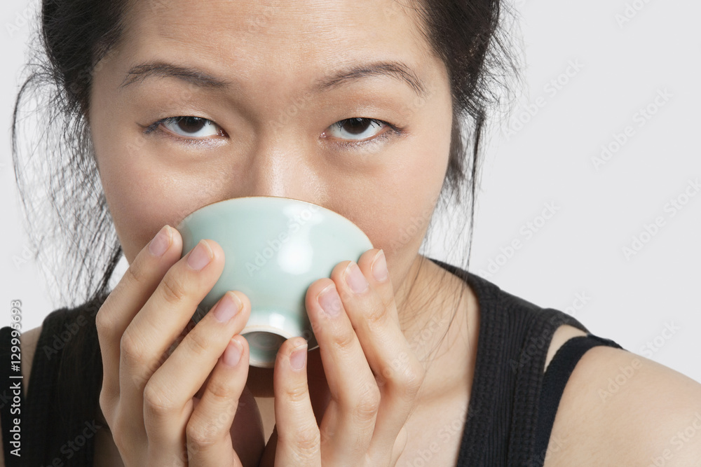 Portrait of a young woman drinking from bowl over light gray background Portrait of a young woman drinking from bowl over light gray background