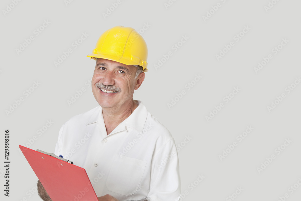 Portrait of happy senior constructor with clipboard over gray background Portrait of happy senior constructor with clipboard over gray background