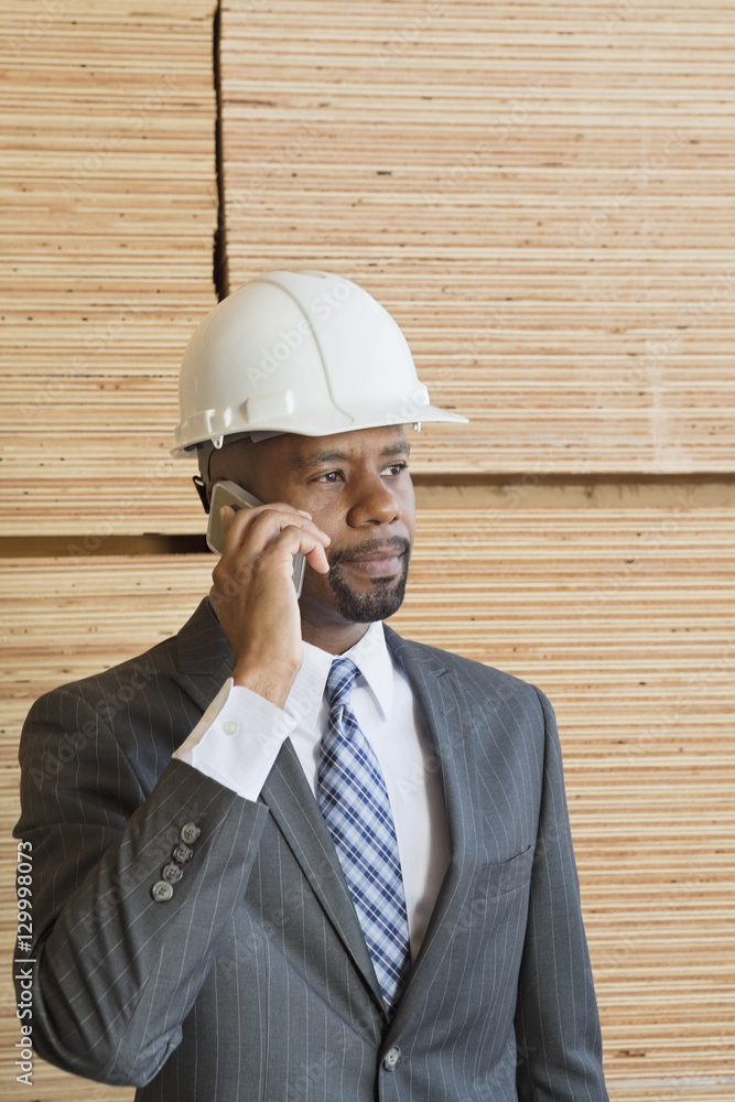 African American male engineer on phone call with stacked wooden planks in background African American male engineer on phone call with stacked wooden planks in background