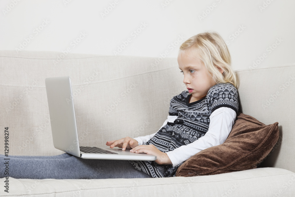 Side view of young girl using laptop on sofa Side view of young girl using laptop on sofa