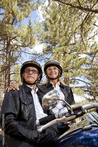 Senior couple wearing helmets stand next to motorcycle