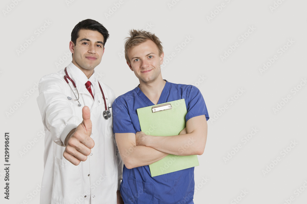 Portrait of an Indian doctor gesturing thumbs up while standing with male nurse over light gray background Portrait of an Indian doctor gesturing thumbs up while standing with male nurse over light gray background