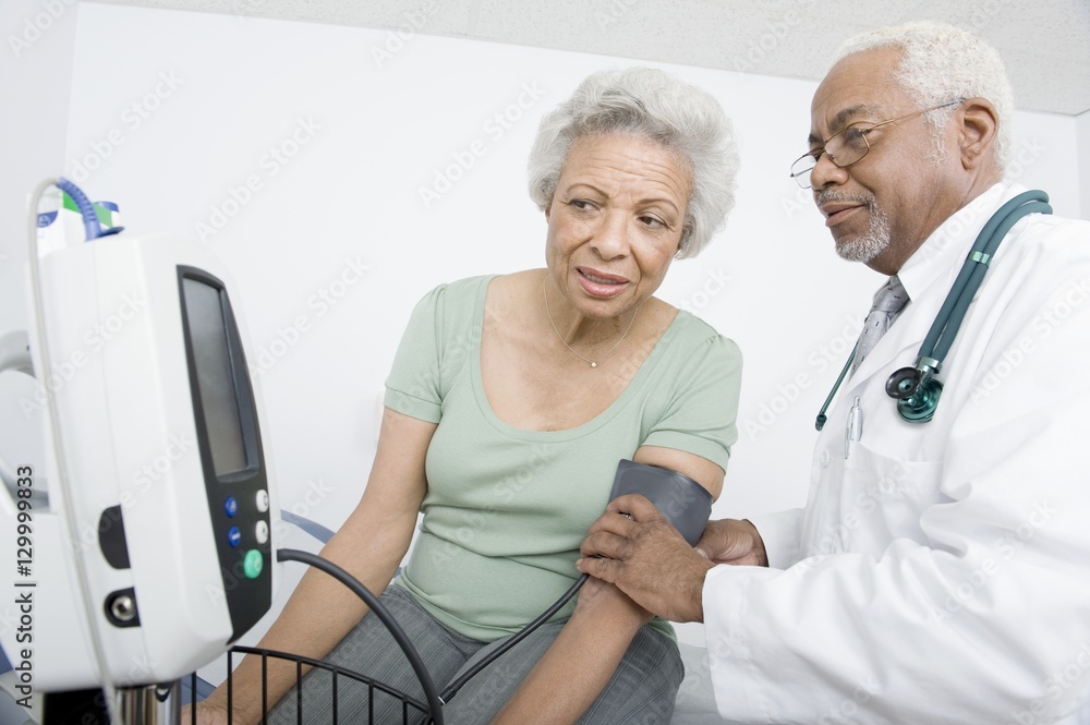 Male doctor checking patient's blood pressure while looking at machine at clinic Male doctor checking patient's blood pressure while looking at machine at clinic