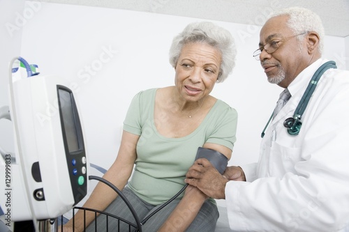 Male doctor checking patient's blood pressure while looking at machine at clinic