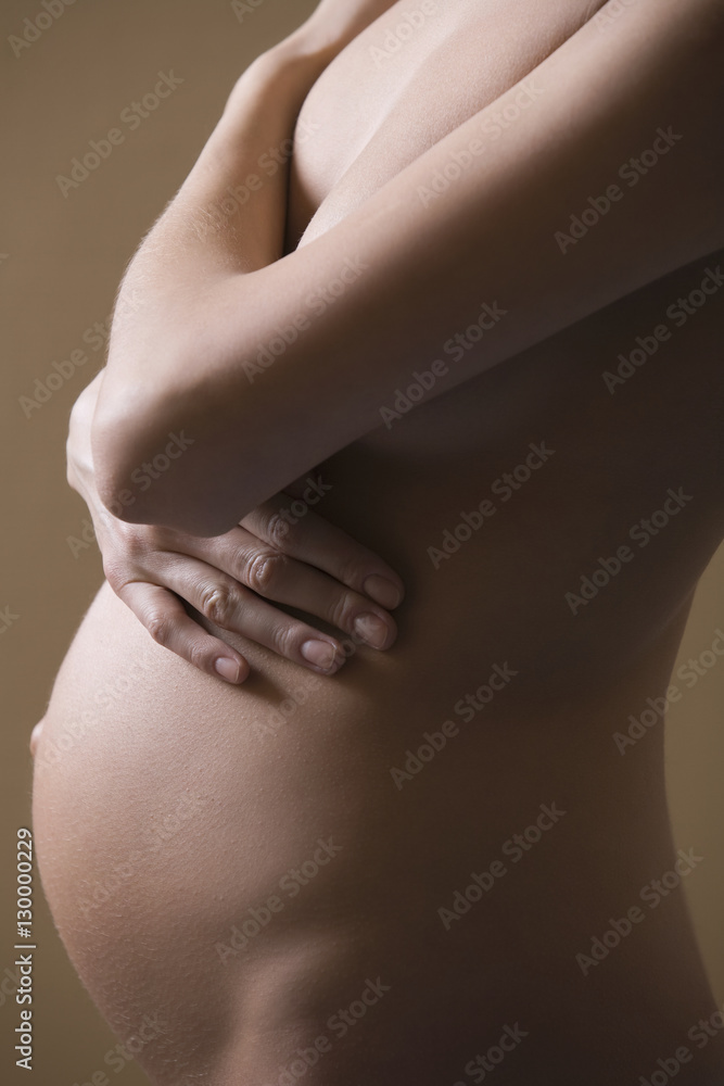 Midsection side view of naked pregnant woman covering breast on colored background