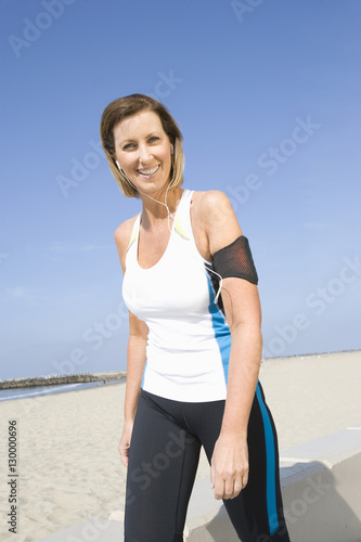 Portrait of a happy woman in sportswear listening music while walking on beach
