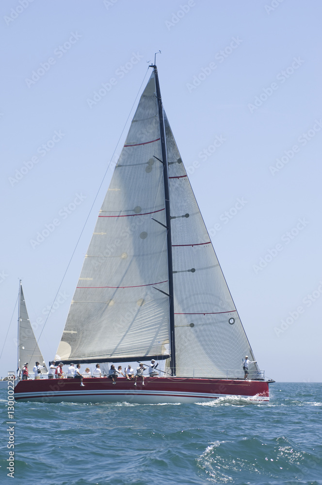 Group of crew members sitting on the side of a sailboat in the ocean Group of crew members sitting on the side of a sailboat in the ocean
