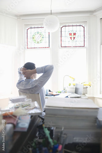 Rear view of businessman relaxing at desk in home office