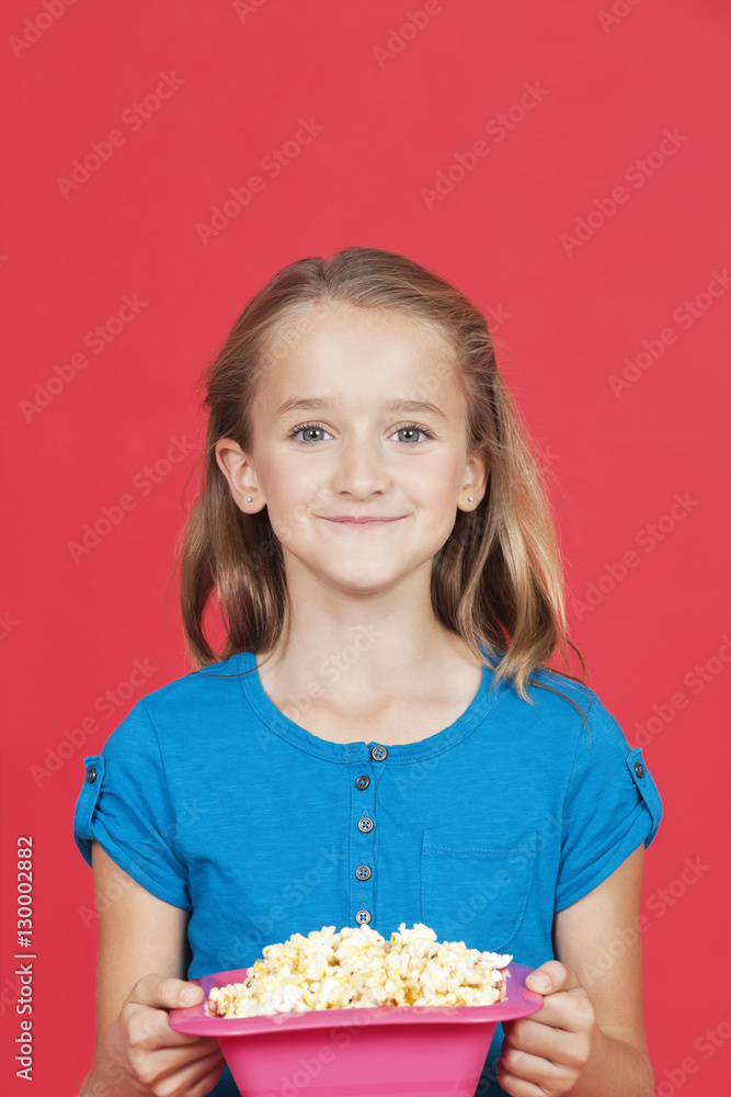 Portrait of young girl holding popcorn container against red background Portrait of young girl holding popcorn container against red background