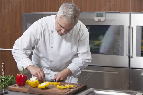 Male chef slicing bell pepper in commercial kitchen