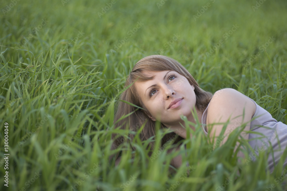 Thoughtful young woman looking up while lying on grass Thoughtful young woman looking up while lying on grass