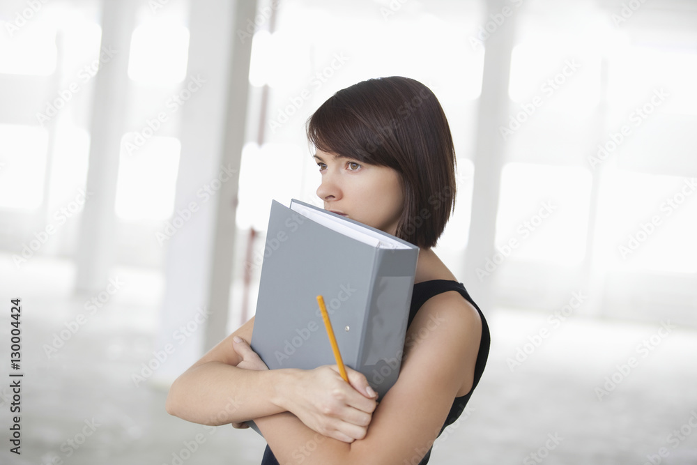 Thoughtful young businesswoman with ring binder in empty warehouse