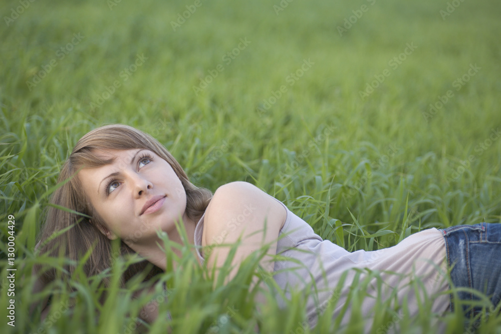 Thoughtful young woman looking up while lying on grass Thoughtful young woman looking up while lying on grass