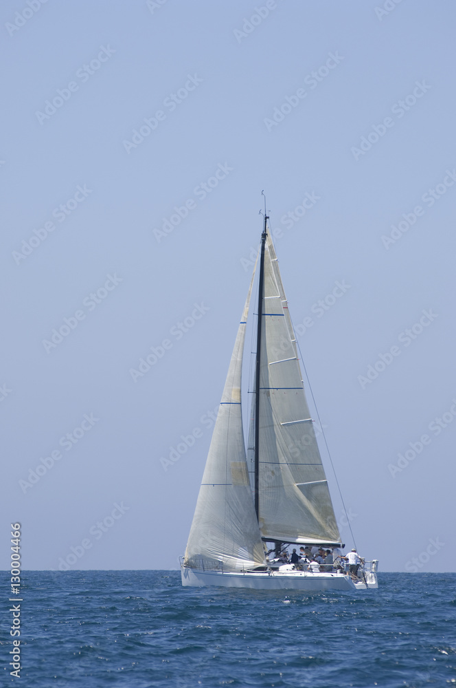 Sailboat racing in the blue and calm ocean against sky Sailboat racing in the blue and calm ocean against sky