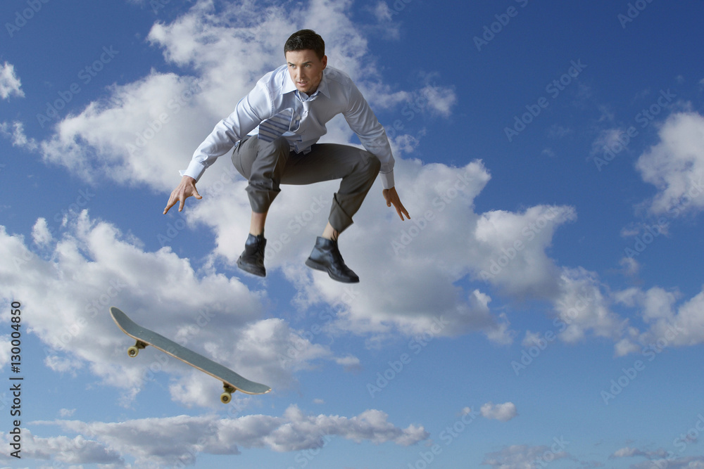 Young businessman performing skateboarding trick in mid-air against cloudy sky Young businessman performing skateboarding trick in mid-air against cloudy sky