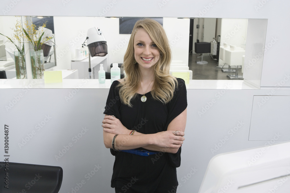 Portrait of happy young hairstylist standing arms crossed at reception in salon Portrait of happy young hairstylist standing arms crossed at reception in salon