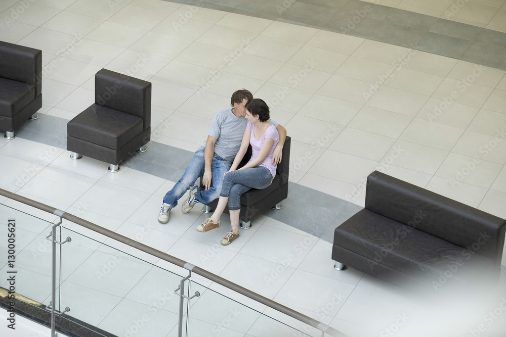 High angle view of romantic young couple sitting on chair in shopping mall High angle view of romantic young couple sitting on chair in shopping mall