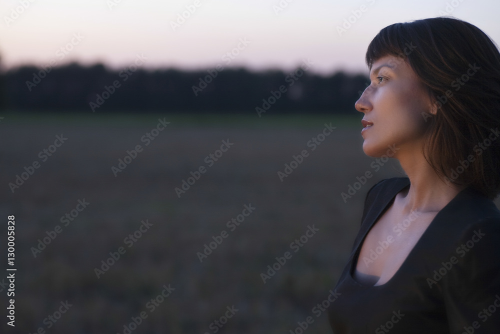 Side view of young woman looking away in field at twilight