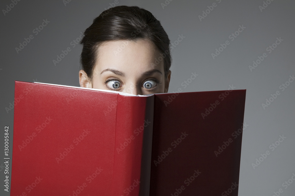 An astonished young female reading book with eyes wide open isolated over grey background An astonished young female reading book with eyes wide open isolated over grey background