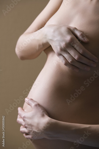 Midsection of naked pregnant woman covering breast and tummy on colored background
