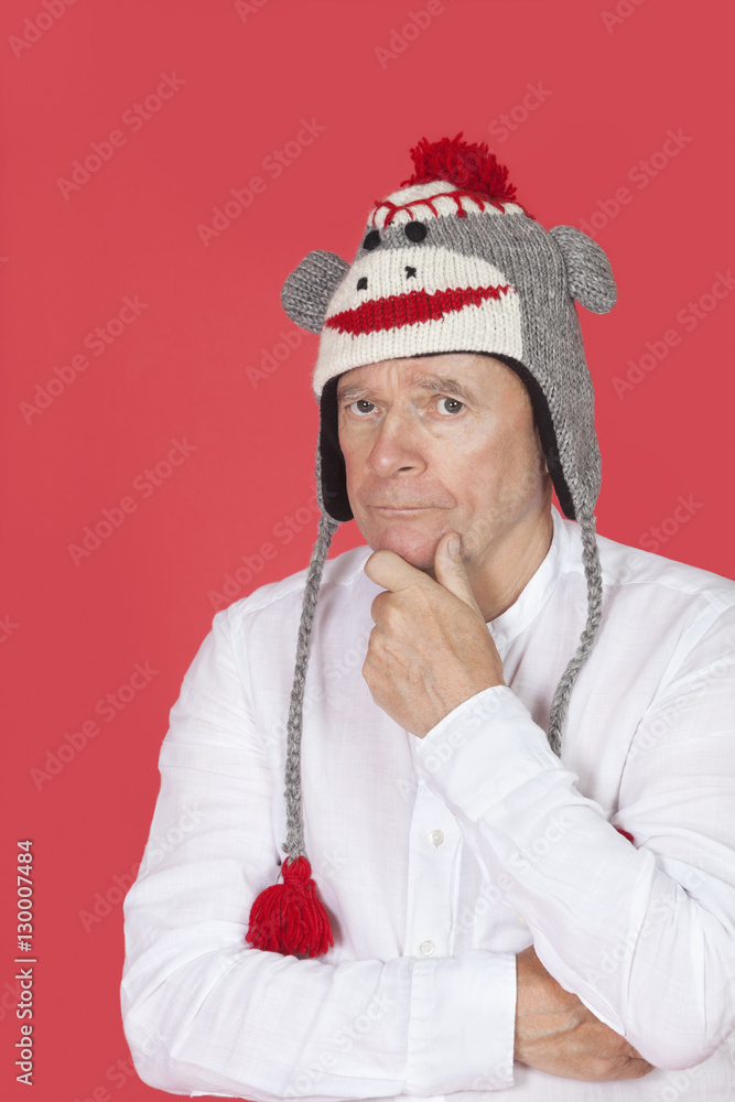 Portrait of thoughtful senior man with hand on chin against red background