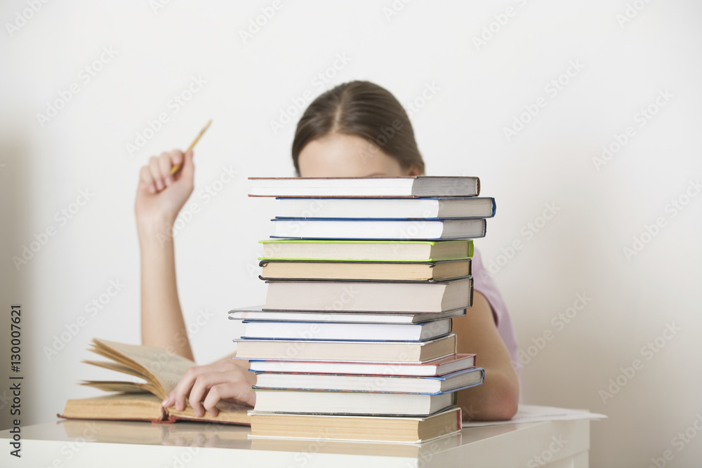 Young woman reading book behind stack of books at home Young woman reading book behind stack of books at home
