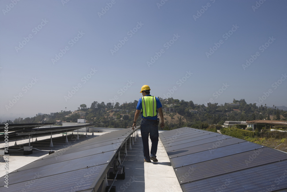 Full length rear view of maintenance worker inspecting solar panels on rooftop
