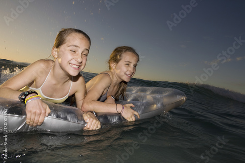 Young twin girls paddling out to sea on air mattress