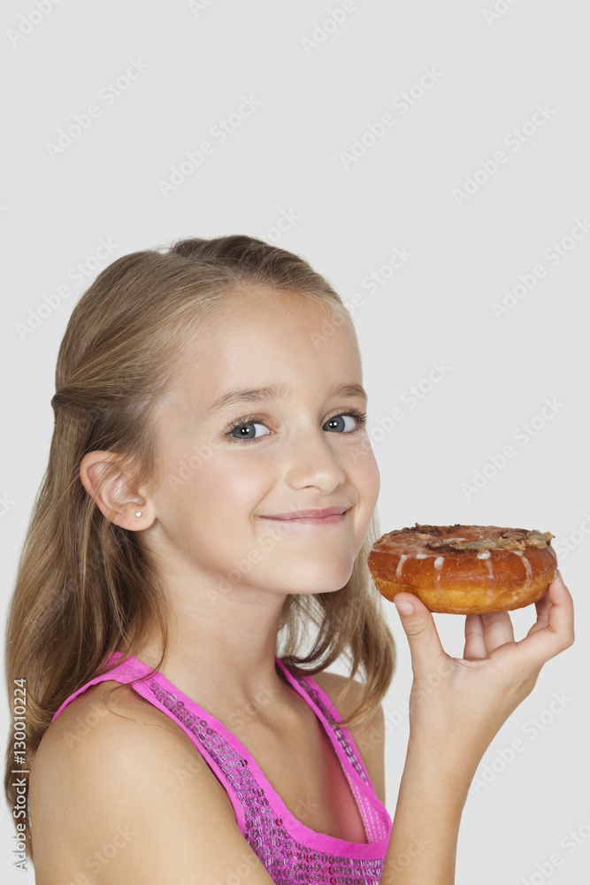 Portrait of young girl holding donut against gray background
