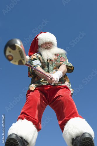 Low angle view of Santa Claus holding golf club against blue sky