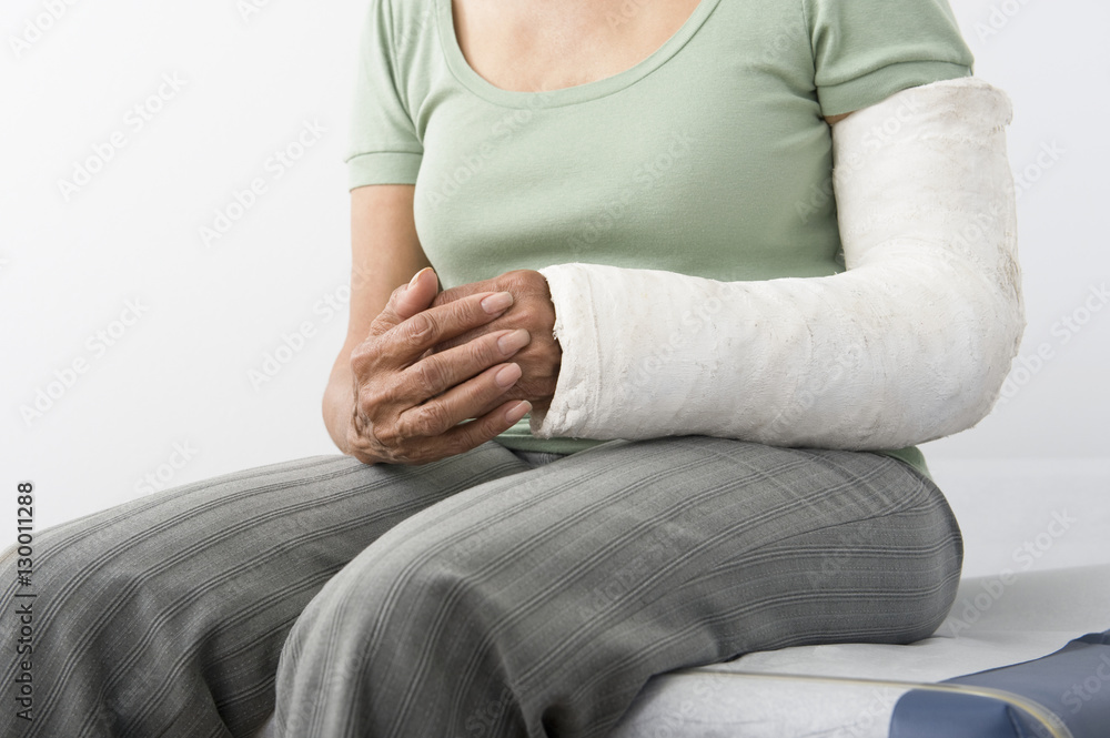 Midsection of a female with fractured hand sitting on bed at clinic