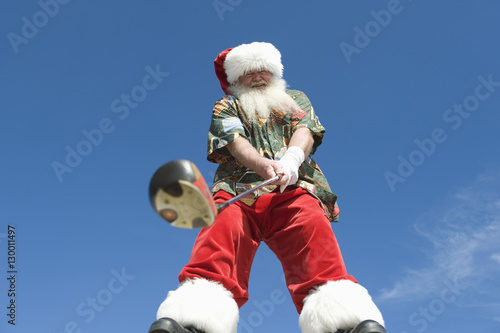 Portrait of happy senior Santa Claus with golf club against blue sky