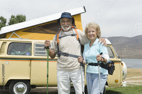 Portrait of a happy senior couple with walking poles and campervan in the background