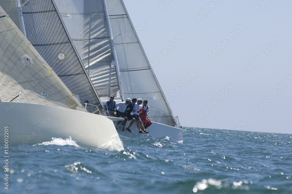 Naklejka premium Group of crew members sitting on the side of a sailboat in the ocean