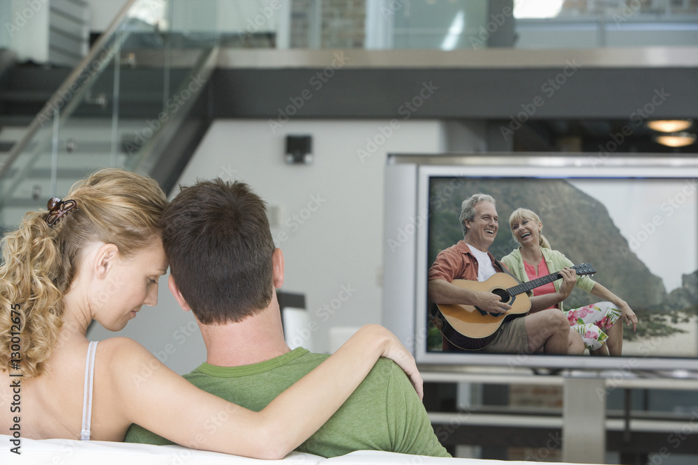 Rear view of young couple watching television in living room Rear view of young couple watching television in living room