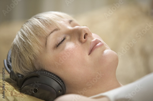 Closeup of beautiful young woman with eyes closed listening music through headphones at home
