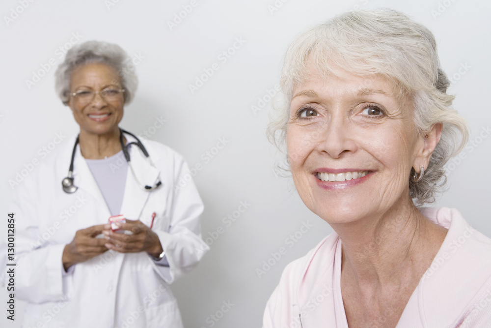 Portrait of happy female patient with doctor holding mobile phone in the background Portrait of happy female patient with doctor holding mobile phone in the background