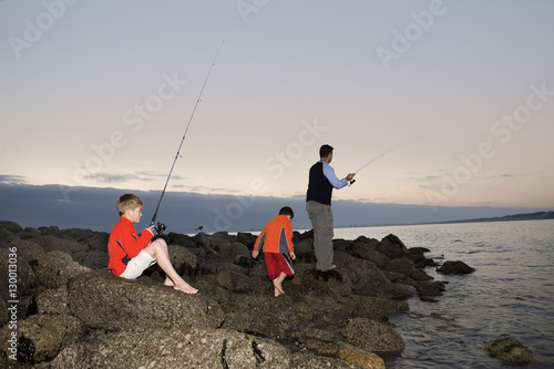 Father and sons fishing by lake at dusk