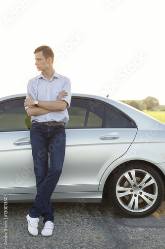 Full length of young man looking away while standing by car at countryside © moodboard