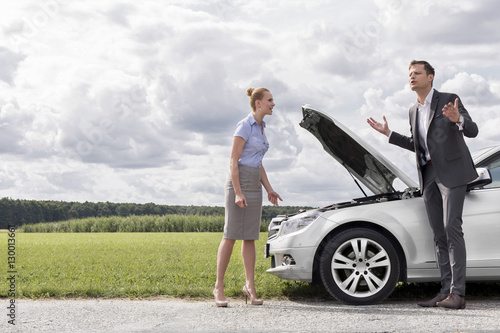 Full length of business couple having argument by broken car at countryside © moodboard