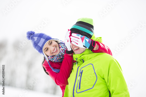 Smiling young woman covering man's eyes in winter