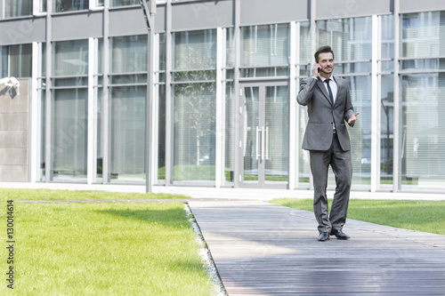 Businessman using cell phone while walking on path outside office
